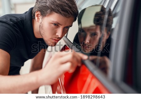 Male customer searching scratches on window of modern vehicle while choosing new car in showroom Royalty-Free Stock Photo #1898298643
