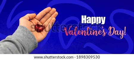 Happy Valentine's Day banner with text inscription and hand with red love heart on a blue background photo