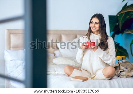 Good day. Dark-haired woman with a red cup in her hands looking relaxed