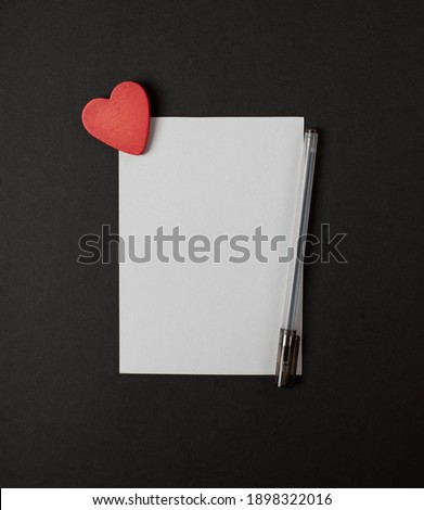 A sheet of paper with a pen and red heart  on the dark (black) background. Romantic love letter for the Valentine's day concept. Space for text.