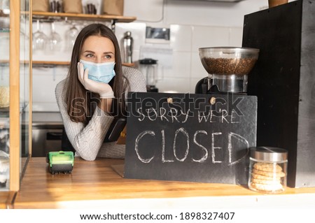Frustrated female owner wearing medical mask leaned on bar counter in closed cafe, small business lockdown due to coronavirus, bankrout concept