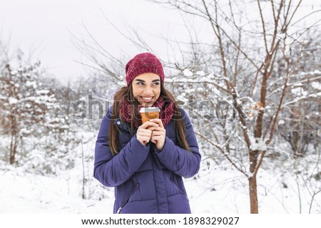 Pretty young woman in winter outfit holding disposable cup filled with hot coffee or tea. Girl holding mug of hot beverage in her hands and walks outdoors in winter.