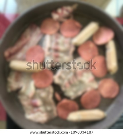 A blurry picture of a beef slice, meat, and sausage on top of a pan