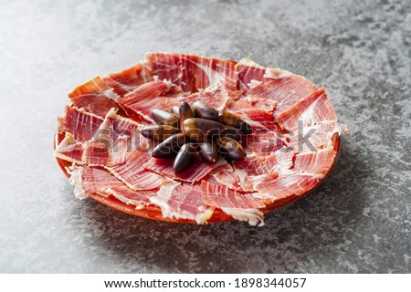 Top view of jabugo ham slices with acorns, Dry Spanish ham, Italian Prosciutto or Parma ham. Black background Royalty-Free Stock Photo #1898344057