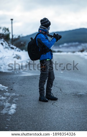 Person taking pictures in the snow on a road in a forest