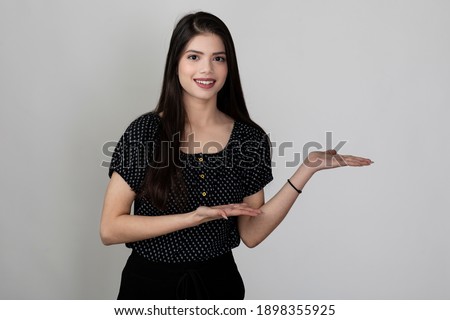 Image of a pretty young girl standing against white background with hands pointing, advertising concept, copy space for text.