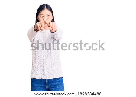 Young beautiful chinese woman wearing casual sweater rejection expression crossing fingers doing negative sign 