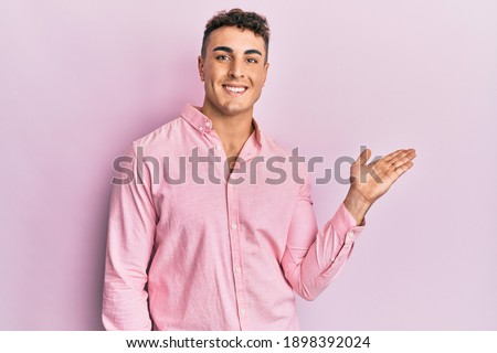 Hispanic young man wearing casual clothes smiling cheerful presenting and pointing with palm of hand looking at the camera. 