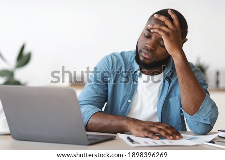 Stressed Black Male Entrepreneur Having Problems At Work. Depressed African American Man Sitting Upset At Desk With Laptop In Office And Touching Head In Despair, Closeup Shot With Free Space Royalty-Free Stock Photo #1898396269