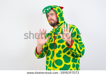 Afraid Young caucasian man wearing a pajama standing against white background, makes terrified expression and stop gesture with both hands saying: Stay there. Panic concept.