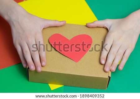 
The child cuts red hearts out of paper with scissors and makes a gift. Close-up. Colored background. Place for an inscription.