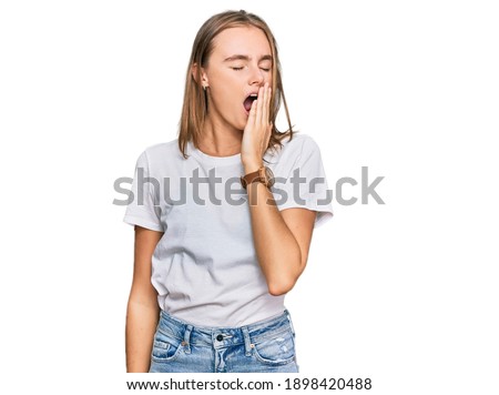 Beautiful young blonde woman wearing casual white t shirt bored yawning tired covering mouth with hand. restless and sleepiness. 