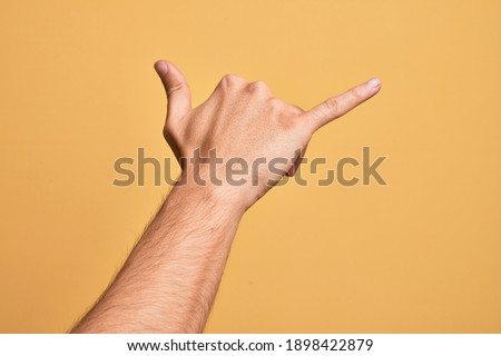 Hand of caucasian young man showing fingers over isolated yellow background gesturing Hawaiian shaka greeting gesture, telephone and communication symbol