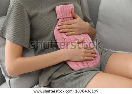 Woman using hot water bottle to relieve menstrual pain on sofa at home, closeup Royalty-Free Stock Photo #1898436199