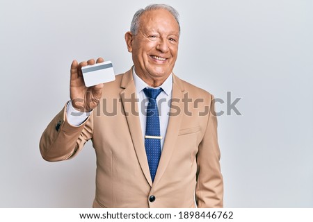 Senior caucasian man holding credit card looking positive and happy standing and smiling with a confident smile showing teeth 