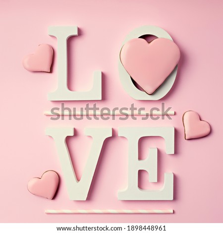 Word Love decorated with heart shaped cookies and straws on pink background. Modern Valentine's Day, dating, romantic or love concept. Creative greeting card layout. Flat lay, top view.