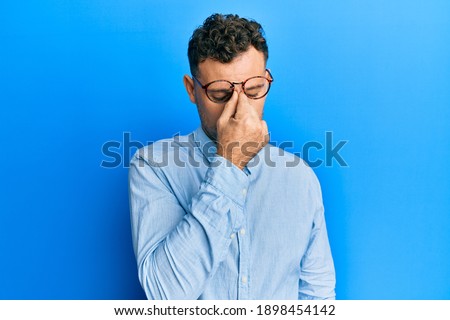 Young hispanic man wearing casual clothes and glasses tired rubbing nose and eyes feeling fatigue and headache. stress and frustration concept. 
