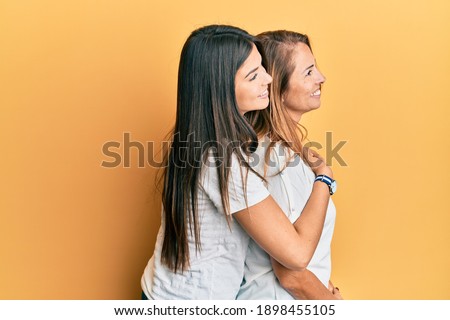 Hispanic family of mother and daughter wearing casual white tshirt looking to side, relax profile pose with natural face and confident smile. 
