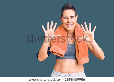 Young woman with short hair wearing sportswear and towel using smartphone showing and pointing up with fingers number ten while smiling confident and happy. 