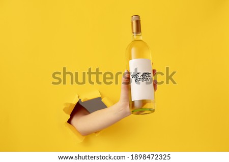 Human hand holding bottle of wine with collar open isolated on yellow background