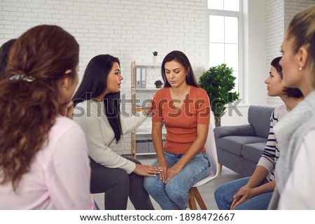 You are not alone. Women helping sad young woman who's been victim of emotional abuse and domestic violence, comforting her and showing their solidarity in support group meeting or therapy session Royalty-Free Stock Photo #1898472667