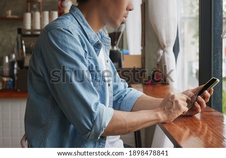 Right View Young Asian Casual Businessman in Denim or Jeans Shirt Using Smartphone in Coffee Shop. Casual Businessman Working with Technology