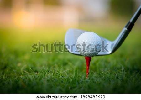High-quality golf club hitting a white golf ball placed on a red peg with green grass.