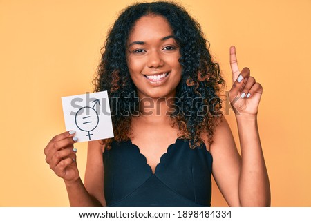 Young african american woman holding we are equal paper smiling with an idea or question pointing finger with happy face, number one 