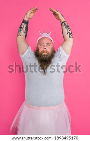 Funny fat man pretending to be a ballerina with tutu - Comic character with beard and tattooes dancing on a pink background Royalty-Free Stock Photo #1898495170