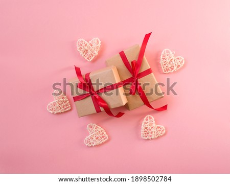 Gifts decorated with red ribbon, pink background, copy space. Two present boxes surrounded with white wicker heats, top view. Valentine or love, spring holidays, Christmas and birthday concept.