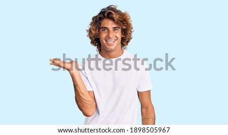 Young hispanic man wearing casual white tshirt smiling cheerful presenting and pointing with palm of hand looking at the camera. 