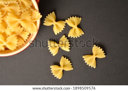 Uncooked farfale butterfly pasta scattered on dark background