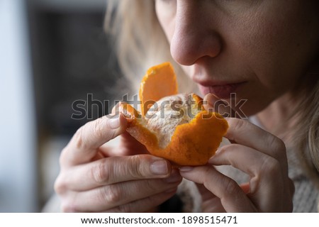 Sick woman trying to sense smell of fresh tangerine orange, has symptoms of Covid-19, corona virus infection - loss of smell and taste, standing at home. One of the main signs of the disease. Royalty-Free Stock Photo #1898515471