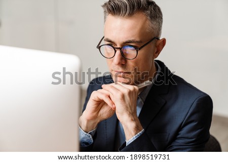 Focused grey man working with computer while sitting at table in office