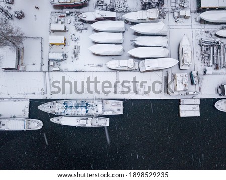Snow-covered barges in the industrial port. Snowy day, blizzard. Aerial drone view.