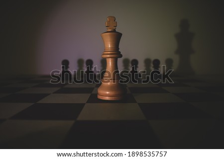 White king in the middle of the board with black pawns and shadows in the background