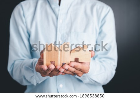 Real estate agent holds a wood house to exchange with his client after signing a home purchase contract, idea for real estate, moving or renting a property.