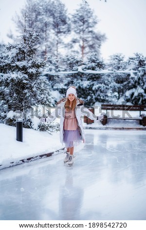 The girl is skating on ice in the forest. Skating rink on the background of the winter forest. Selective focus photo