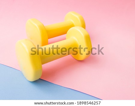 Yellow dumbbell color on pink, blue and yellow mat. Design of a sports poster or banner in fashionable colors of 2021