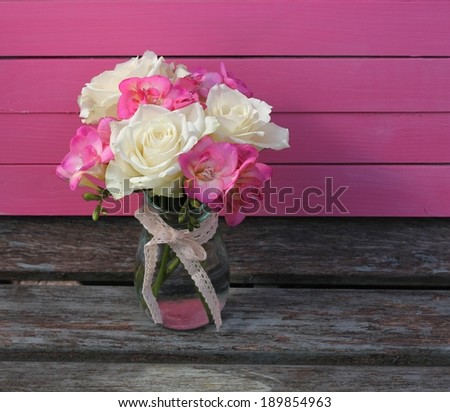 Pretty posy of cream roses and pink fuchsia in a glass jam jar tied with cotton lace ribbon, stood on a vintage wooden bench, shabby chic image 