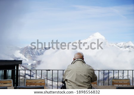       
The old man looks at the snow-capped mountains in the distance                         