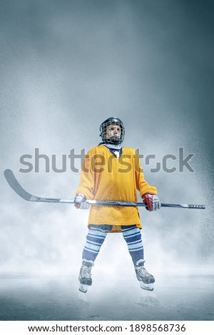 Champion. Little hockey player with the stick on ice court and smoke background. Sportsboy wearing equipment and helmet training in action. Concept of sport, childhood, motion, movement, action.