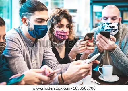 Worried people with face mask checking news on mobile smart phones at coffee break - New normal lifestyle concept with milenials on contact tracing app - Bright azure filter with focus on left guy Royalty-Free Stock Photo #1898585908