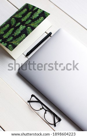Laptop with notebook paper, a pen and with glasses on white wooden table. A lot of equipment for working. Workflow
