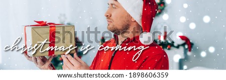 panoramic shot of man in santa hat holding gift box, christmas is coming illustration