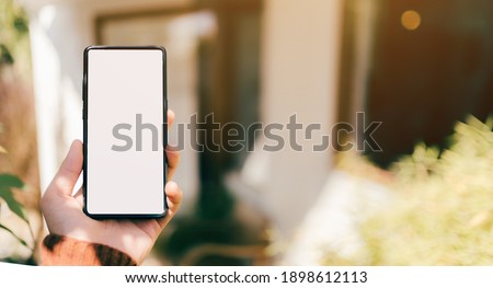 A man hand with red sweater are holding a mockup of vertical black 5g mobile smartphone with blank white screen for insert your design, digital global communicate by smart phone, clipping path include