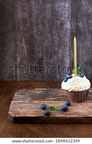 Cupcake with a blueberry and a candle. Birthday cupcake. Blueberry. Blue, brown. Wooden background. Close-up, Side View.