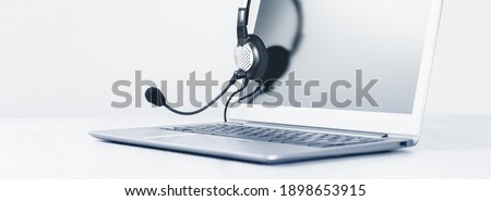 Laptop. Mockup screen and headphones on grey desk and plain background wide banner. Distant learning or working from home, online courses or support minimal concept. Helpdesk or call center headset Royalty-Free Stock Photo #1898653915