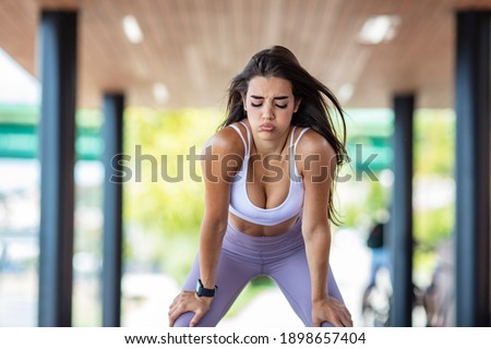 Beautiful young woman resting outdoor after exercise. Tired female runner walking.She is exhausted of running. Young woman making pause after exercising in an urban park