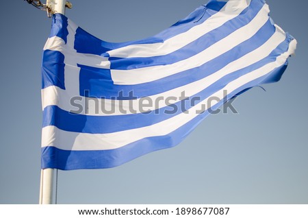 Photo of blue and white greek national flag waving under a blue sky on a sunny day